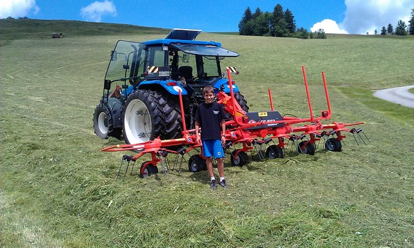 Трактор Нью Холланд на луге с ворошителем сена Kuhn GF 582. Сдвоенные колеса помогают не утрамбовывать траву и почву